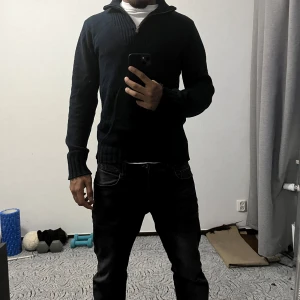 Mörkblå stickad tröja med half zip - Mörkblå stickad tröja med half zip och hög krage. Tröjan har långa ärmar och ribbade muddar vid ärmslut och nederkant. Perfekt för dig som gillar en enkel och stilren design.