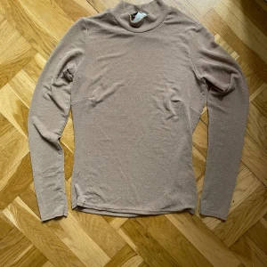 Beige glittrig polotröja från NLY Trend - Säljer en beige polotröja från NLY Trend i storlek S. Tröjan har ett glittrigt material som ger en snygg shimmer-effekt och är långärmad med en tight passform. En aning see trough och stretchigt skönt material
