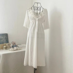 Vit klänning med spetsdetaljer - Romantisk vit klänning med vacker spets runt halsringningen och ärmsluten. Lite genomskinlig. Passar perfekt som sovplagg. Har en liten fläck på framsidan (sista bild). Storlek: S (34-36). Dockans storlek: 34.