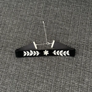 Svart sammetschoker med blommor - Snygg svart choker i sammet med silverfärgade detaljer och blommor av glittriga stenar. Halsbandet har justerbar kedja och blommönster i mitten, perfekt för att ge din outfit en cool och elegant touch.