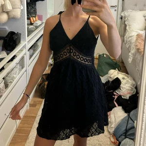 Svart spetsklänning med öppen rygg - Supersnygg svart kortklänning med spetsdetaljer och v-ringad front. Köpt i Italien!! Klänningen har tunna axelband som knyts i nacken och en öppen rygg för extra wow-effekt. 