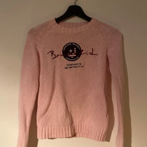 Ljusrosa stickad tröja från Bondelid - Säljer en ljusrosa stickad tröja från Bondelid i storlek XS. Tröjan har rund hals, ribbade muddar och ett broderat Bondelid-tryck med patch framtill. Mjuk och skön kvalitet, perfekt för kyliga dagar. Klassisk och enkel design med lång ärm.