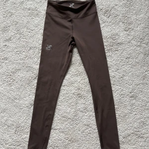Bruna leggings från RevolutionRace XS - Snygga bruna leggings från RevolutionRace i storlek XS. De är högmidjade och har en tight passform, perfekta för träning eller chill. Tillverkade i mjukt och stretchigt syntetmaterial med logga på benet och bak. Supersköna och stilrena!