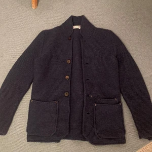 Stickad Cardigan/kofta från Gran Sasso - Säljer en mörkblå stickad cardigan jacka från Gran Sasso. Jackan har grovstickad struktur, stora bruna knappar och två rejäla fickor framtill. Knappen längst ner saknas men inget som syns vid användning. Kom pm för bild med den på.