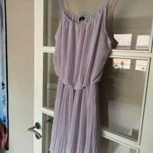 Ljuslila plisserad klänning Bik Bok - Supersöt ljuslila klänning från Bik Bok med tunna axelband och plisserad kjol. Den har ett flowy fall och ärmlös design som ger en chill och feminin vibe. Perfekt för varma dagar och har en mjuk, luftig känsla tack vare det tunna materialet.