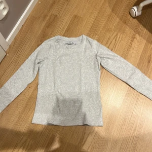 Ljusgrå långärmad tröja 157 - En basic ljusgrå långärmad tröja från 157. Tröjan har rund halsringning och är i mjuk bomull, perfekt för lager-på-lager. Enkel och clean stil som funkar till allt. Snygg att matcha med jeans eller kjol.