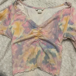 Pastellfärgad ribbad topp från Monki - Superfin ribbad topp från Monki i storlek L men är liten i passform, pastellfärgat mönster i rosa, gul, blå och lila. Toppen har v-ringning, rynkade detaljer framtill och korta ärmar. Perfekt för dig som gillar färg och en unik look!