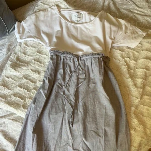 Vit och grå kortklänning från Monrow - Supersöt kortklänning från Monrow i storlek XS. Överdelen är vit med rund hals och korta ärmar, medan kjoldelen är ljusgrå med en rynkad midja och knytband. Väldigt fint skick utan defekter! Nypris ca 700 kr