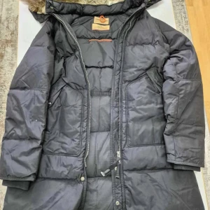 Svart lång dunjacka från Parajampuer  - Lång svart dunjacka från Polar Campers med stor huva fodrad i mjuk äkta päls. Jackan har två stora fickor framtill, dragkedja och tryckknappar. Perfekt för kalla vinterdagar och riktigt varm med sin quiltade design och pälsdetaljer. Jag köpte den för 10000 tusen och vill sälja den för 3500 den är äkta 