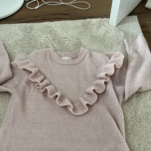 Ljusrosa stickad tröja med volang - Supersöt ljusrosa stickad tröja från Gina Tricot i storlek 158/164. Tröjan har ett vågigt mönster och en bred volang som går över bröstet och axlarna. Rund halsringning och långa ärmar. Perfekt för dig som gillar gulliga detaljer och mjuka material.