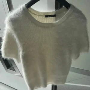 Vit fluffig stickad tröja Gina Tricot - Supermjuk och fluffig vit stickad tröja från Gina Tricot med korta ärmar och rund hals. Perfekt för dig som gillar en cozy vibe och vill ha något som känns extra mjukt mot huden. Enkel att styla med jeans eller kjol för en chill look.