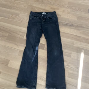 Svarta bootcut jeans med fickdetaljer - Snygga svarta jeans med bootcut passform och coola fickdetaljer med knappar både fram och bak. Jeansen har låg midja och är tillverkade i mjukt denimtyg som sitter skönt. Perfekta för dig som gillar en klassisk men trendig look.