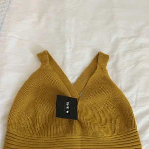 Gul ribbad stickad linnetopp från SHEIN - Snygg gul stickad linnetopp från SHEIN med ribbad struktur och breda axelband som korsas i ryggen. Toppen har en croppad passform och djup v-ringning framtill. Perfekt för att ge din outfit en cool och trendig vibe.