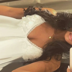 Vit topp med spets och satin - Supersöt vit topp med tunna axelband och v-ringad spets upptill. Spetsen har blommiga detaljer och resten av klänningen är i glansigt satinmaterial. Perfekt för dig som gillar romantisk och feminin stil.