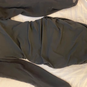 Svart långärmad klänning med mesh - Snygg svart långklänning med långa ärmar och meshdetaljer. Klänningen har en figurnära passform och är tillverkad i ett mjukt syntetmaterial som ger en cool och modern look. Perfekt för dig som gillar stilrena och minimalistiska plagg.