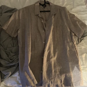 Beige linneskjorta från H&M, L - Säljer en beige kortärmad skjorta från H&M i storlek L. Skjortan är i svalt linnematerial, har klassisk krage, bröstficka och knäppning framtill. Perfekt för varma dagar och enkel att styla till jeans eller shorts.