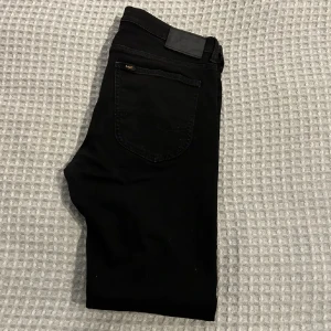 Svarta jeans från Lee - Snygga svarta jeans från Lee med klassisk femficksdesign och diskret Lee-logga på bakfickan. Jeansen har en stilren look och passar perfekt till en streetwear-outfit. Materialet är mjukt och följsamt för en bekväm känsla hela dagen.