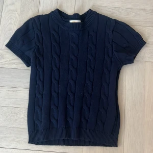 Mörkblå stickad tröja Gina Tricot - mörkblå stickad tröja från Gina Tricot med korta ärmar och grov kabelstickning. Rund hals och ribbade muddar