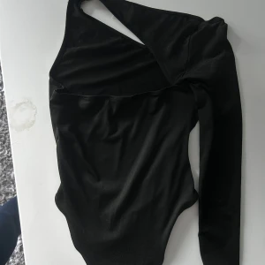 Svart oneshoulder topp! - Säljer en svart, tight och stilren oneshoulder topp med lång ärm. Toppen har en asymmetrisk design som är snyggt att använda till ett par jeans osv!! Den har inga defekter då jag använt den vid ett tillfälle tidigare!!