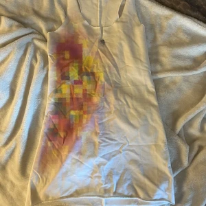 Vit mini klänning från MET med färgblock - Säljer en vit mini klänning från MET i storlek S. Klänningen har ett färgglatt blockmönster i rosa, gul och lila på framsidan och en liten metall-detalj vid halsringningen. Ärmlös och med sportig racerback, perfekt för dig som gillar unika detaljer.