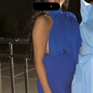 Kornblå långklänning med volang - Säljer en kornblå långklänning med figurnära passform och snygga volangdetaljer upptill. Klänningen har ärmlös design och en elegant siluett som ger en stilren look. Perfekt för dig som vill sticka ut med färg och form. Använd endast i några timmar 