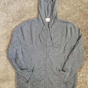 Kashmir zip från Zara - Mjuk och chill grå hoodie från Zara Basic med dragkedja hela vägen, huva med snörning och två fickor framtill. Tröjan är långärmad och har ribbade muddar vid ärmslut och nederkant. Perfekt för sköna dagar och enkel att matcha med jeans eller joggers.