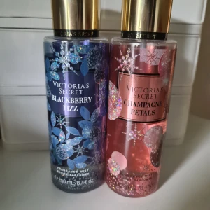 Victoria's Secret 2 bodymists blackberry fizz och champagne petals - Två parfymmister från Victoria's Secret: Blackberry Fizz i blå/lila flaska med glittriga blommor och Champagne Petals i rosa flaska med holografiska detaljer. Båda har guldiga lock och rymmer 250 ml. Doftnoter av bär, champagne och blommor. Den rosa (champagne petals) har mindre än halva kvar och den blåa misten har mycket kvar- se bilder och avgör själva. Säljes tillsammans och förhandlar ej med priset 