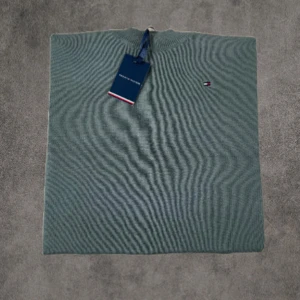 Olivgrön stickad tröja Tommy Hilfiger - Snygg olivgrön stickad tröja från Tommy Hilfiger med diskret logga på bröstet. Tröjan har rund halsringning med ribbade detaljer och är långärmad. Perfekt för dig som gillar stilren och enkel design med en touch av premiumkänsla.