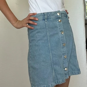 Ljusblå jeanskjol med knappar - Säljer jättefin ljusblå jeanskjol från Divided med silverfärgade knappar framtill💙🦋Perfekt för sommaren och snygg både till vardags och fest