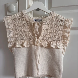 Beige spetsblus från Zara med volang - Supersöt blus från Zara i beige med stickad botten och spets upptill. Volangdetaljer vid axlar och hals, samt knytband framtill. Luftigt spetsmönster och romantisk vibe, perfekt för dig som gillar detaljer. Storlek s men är mindre och kortare