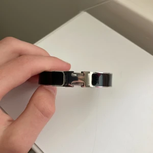 H-armband  - Snyggt svart armband  med den ikoniska H-detaljen i silverfärgad metall. Armbandet har en stilren och modern design med blank finish och är perfekt för dig som gillar exklusiva accessoarer med statement-känsla.