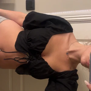 Svart croppad blus med snörning - Supersnygg svart blus med puffiga offshoulder-ärmar och croppad passform. Toppen har snörning framtill som ger en cool detalj och sitter tajt över bysten. Perfekt för dig som gillar trendiga och feminina plagg. Passar bra inför festliga event och sommar! 😇