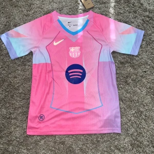 Barcelona Lamine Yamal rosa matchtröja small - Snygg Barcelona fotbollströja från Nike med Lamine Yamal och nummer 10 på ryggen. Tröjan är rosa med inslag av ljusblått och lila, har korta ärmar och coolt grafiskt mönster. Spotify-logga på bröstet och klubbmärke i vitt. Perfekt för dig som älskar Barca och vill sticka ut på planen. Storlek s jag har 2 skriv om ni vill ha båda