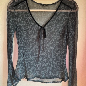 Svart blommig sidenblus från Massimo Dutti - Supersnygg svart sidenblus från Massimo Dutti  med långärmar och svagt mönster i vitt. V-ringad hals med söt knytdetalj framtill i sammet och spetskant vid ärmslut och nederkant. Blusen är lätt transparent och har en slim passform som ger en chic vibe.