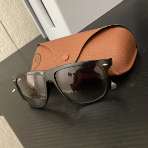 Svarta Ray-Ban boyfriend - Snygga svarta Ray-Ban Wayfarer solglasögon med klassisk fyrkantig form och mörka tonade linser. Bågarna är i svart plast med silverdetaljer vid fronten. Kommer med original Ray-Ban fodral i brunt konstläder. Perfekt för dig som vill ha en ikonisk look. Ny pris 1000 köpta på synsam. Allt og kommer🙏