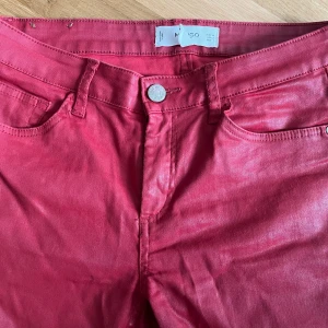 Raka vaxade jeans från Mango, strl 34 - Snygga röda vaxade jeans från Mango i rak modell med klassisk femficksdesign. Byxorna har normal passform och är tillverkade i bomull med en lätt glansig finish. Passar S/34. Bra längd för mig som är 159 cm. 