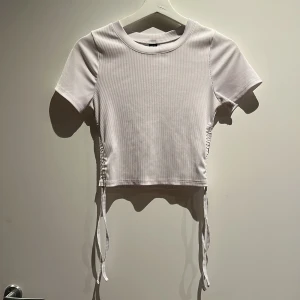 Vit croppad ribbad topp med snörning - Säljer en vit croppad topp med korta ärmar och snygg ribbad struktur. Toppen har snörning i sidorna. 