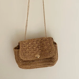 Beige axelväska från H&M med kedja - Snygg beige axelväska från H&M med flätad design och guldfärgad kedja som axelrem. Perfekt storlek och väldigt fin