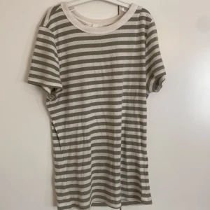 Randig t-shirt från H&M - Snygg t-shirt från H&M i storlek S med horisontella grågröna och vita ränder. Modellen har rund hals och korta ärmar och sitter tight mot kroppen..Perfekt för dig som gillar enkel och stilren design med lite edge.