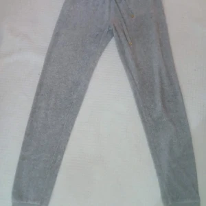 Mjukisbyxor i velour, låg midja, från Juicy Couture - Säljer snygga grå mjukisbyxor i velour med låg midja från Juicy Couture. Nästintill nya, endast använt dom en gång. De har guldfärgade detaljer på snörningen och bakfickor för extra stil. Mjukt material i 90% bomull som känns skönt mot huden. Har en väldigt snygg passform. Perfekta för en chill dag.