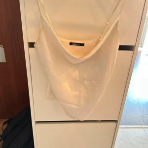 Vit linnetopp från Gina Tricot - Säljer en stilren vit linnetopp från Gina Tricot i storlek 34. Toppen har smala axelband och en snygg draperad halsringning som ger en cool vibe. Materialet känns mjukt och har en lätt glans, perfekt för varma dagar eller när du vill ha en enkel men chic look.