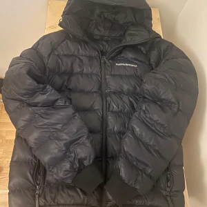 Svart Peak Performance dunjacka M - Säljer en mörkblå dunjacka från Peak Performance i storlek M. Ser lite svart ut ibland. Den har använts en vinter. Den är i väldigt bra skick bara ett liten defekt på luvan som knappt syns. Kostar ungefär 2000kr kronor ny.