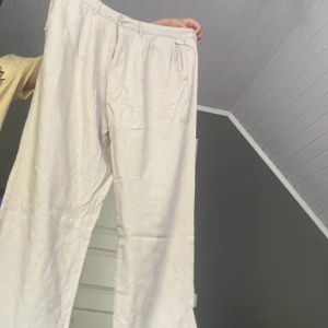 Beige linnebyxor med rak passform - Säljer ett par ljusbeige linnebyxor med rak och relaxed passform. Byxorna har klassiska fickor och hällor för bälte, perfekt för en chill och stilren look. Materialet är linne vilket gör dem luftiga och sköna, särskilt under varmare dagar.
