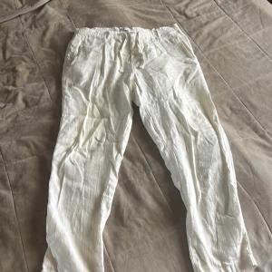 Vita linnebyxor från Zara med snörning - Snygga vita linnebyxor från Zara med avslappnad passform och snörning i midjan. Byxorna har sidofickor och en knappdetalj framtill. Perfekta för chill dagar och sommarhäng, riktigt sköna och luftiga.