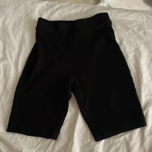 Svarta ribbade cykelshorts från Zara - Svarta cykelshorts från Zara i ribbad, stretchig bomull. De har hög midja och sitter tight, vilket gör dem riktigt snygga och bekväma. Perfekta för att styla med en oversized t-shirt eller hoodie. Passar dig som gillar minimalistisk och clean look.