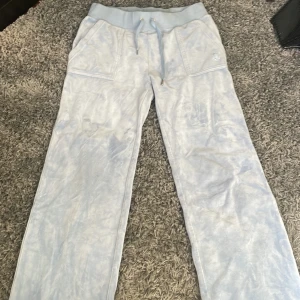 Ljusblå mjukisbyxor Juicy Couture S - Säljer ett par ljusblå mjukisbyxor från Juicy Couture i storlek S. Byxorna har bred resår i midjan med snörning, framfickor och bakfickor med lock och silverfärgade knappar med Juicy-logga. Mjukt och skönt material som ger en chill vibe.