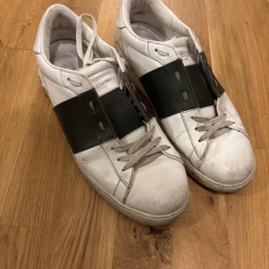 Valentino Garavani Open sneakers vit/svart - Säljer ett par Valentino Garavani Open sneakers i vit skinn med bred mörkgrön läderdetalj över mitten. Klassisk rund tå, platt sula och snörning framtill. Snygg kontrast mellan det vita och mörkgrön, perfekt för dig som gillar stilrena designer.  Skorna är på bilderna smutsiga men dem tvättas ordentligt innan frakt