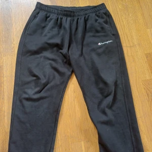 Svarta mjukisbyxor från Champion XL - Svarta mjukisbyxor från Champion i storlek XL. Byxorna har elastisk midja och två sidofickor. Champion-loggan är broderad på vänster lår. Sköna och avslappnade med rak passform, perfekta för chill eller träning.