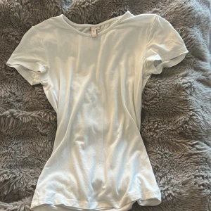 Vit t-shirt från Nelly, storlek S - En clean och enkel vit t-shirt från Nelly i storlek S. Modellen är klassisk med rund hals och korta ärmar, perfekt för en chill och stilren look. Materialet känns mjukt och skönt mot huden, och passformen är normal. Snygg att matcha med jeans eller shorts.