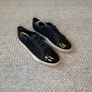 Marinblå Lanvin Sneakers - Snygga svarta sneakers från Lanvin med en cool lackad tå och ovandel i mocka. Skorna har snörning och en vit platt sula som ger en schysst kontrast. Perfekta för dig som gillar stilrena detaljer och vill sticka ut lite extra.